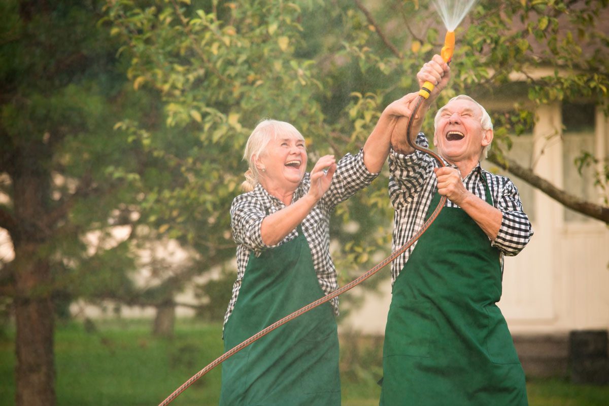 Two elderly people playing with water hose